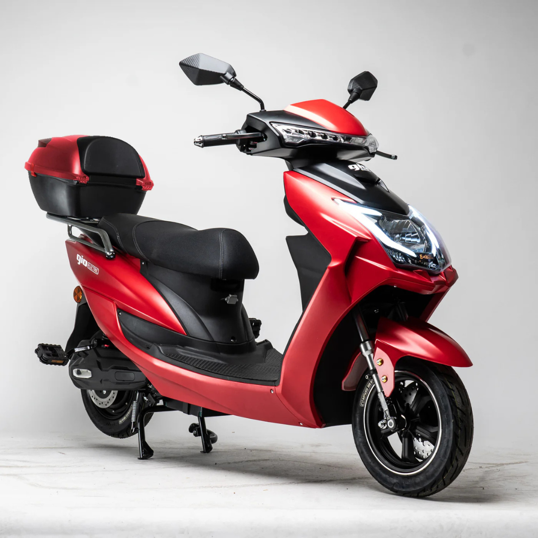 The GIO Phoenix Premium Electric Scooter, featuring a red frame, black seat, and rear storage box, is parked on a white studio background from a front-side angle. This long-range model offers convenient travel without requiring a license.